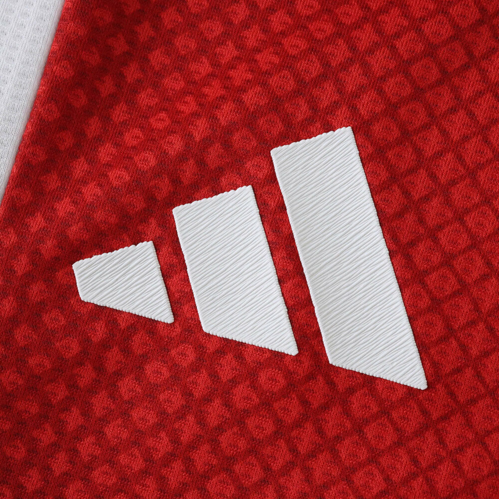 Close-up of the white Adidas logo on the red textured Ajax Home 2025/26 Player Version jersey fabric.