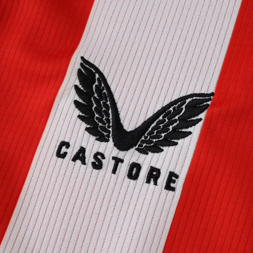 Close-up of the Castore logo on the Athletic Bilbao 2025/26 home fan jersey, red and white stripe background.