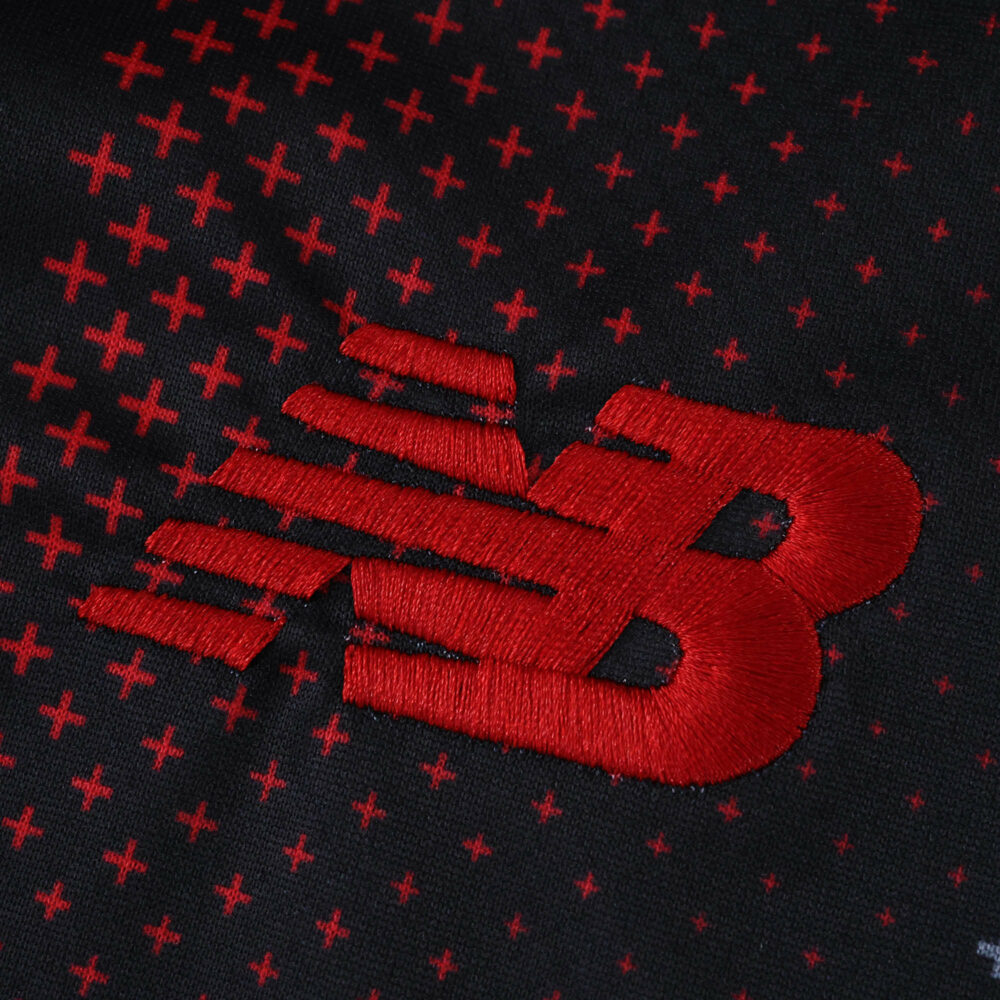 Close-up of the red New Balance logo on the Bayer Leverkusen 2025/26 home fan jersey.