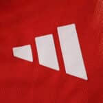 Close-up of the white Adidas logo on the red Bayern Munich 2025/26 home player jersey fabric.