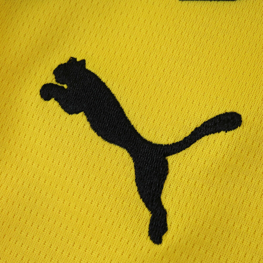 Close-up of the black Puma logo on yellow Borussia Dortmund 2025/26 Home Fan Version jersey fabric.