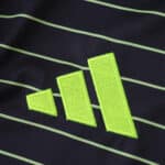 Close-up of lime green Adidas logo on the Celtic Away 2025/26 Fan Version jersey with thin green stripes.