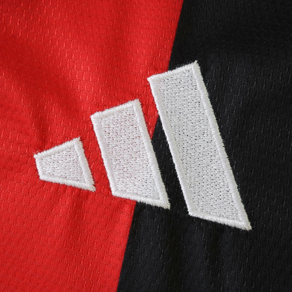 Close-up of the adidas logo on the 2025/26 Eintracht Frankfurt home fan jersey, red and black background.