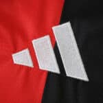 Close-up of the adidas logo on the 2025/26 Eintracht Frankfurt home fan jersey, red and black background.