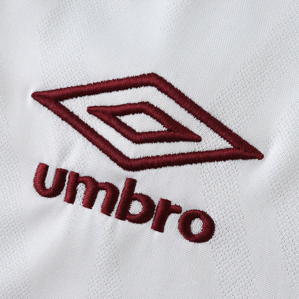 Close-up of maroon Umbro logo stitched on the white Fluminense Away 2025/26 Fan Version jersey fabric.