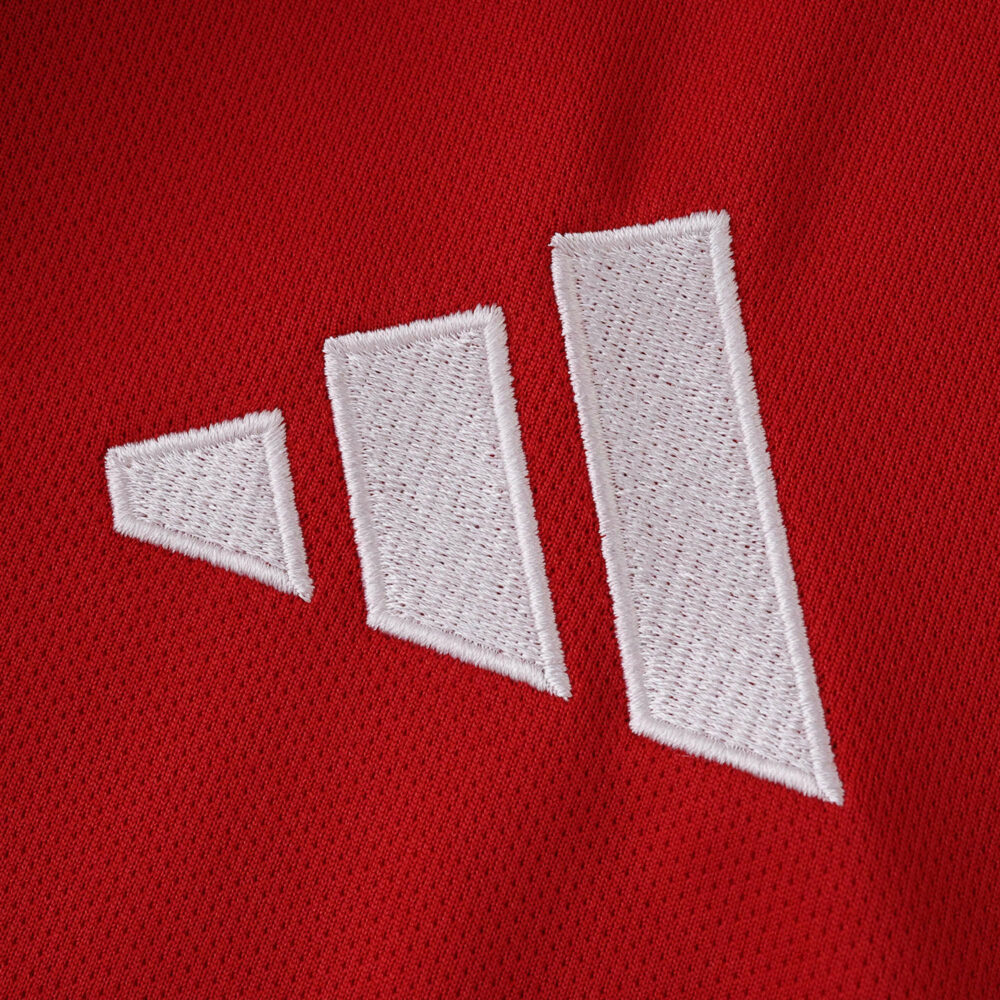 Close-up of the white Adidas logo on the red Manchester United 2025/26 home fan jersey fabric.