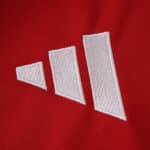 Close-up of the white Adidas logo on the red Manchester United 2025/26 home fan jersey fabric.