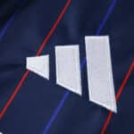 Close-up of Olympique Lyonnais 2025/26 away fan jersey with Adidas logo on dark blue fabric with red and blue stripes.