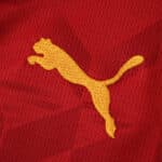 Close-up of the yellow Puma logo on the red Valencia Away 2025/26 Fan Version jersey.