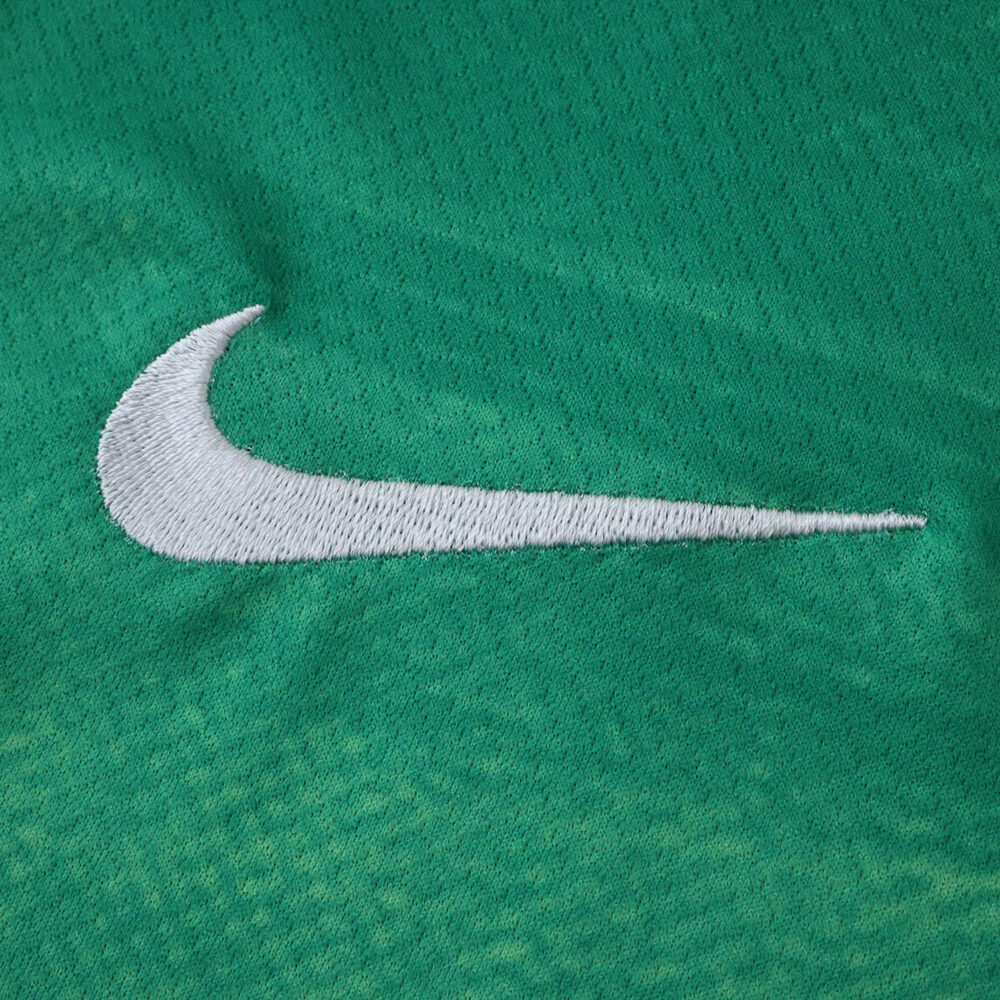 Close-up of the white Nike logo embroidered on the green VfL Wolfsburg 2025/26 home fan jersey.
