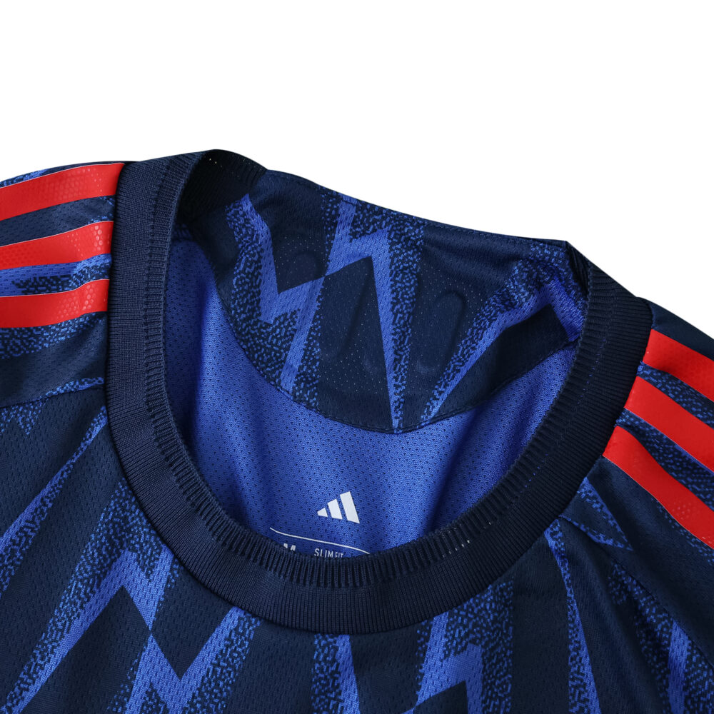 Close-up of Arsenal 2025/26 away player jersey collar with blue zigzag pattern and red shoulder stripes.