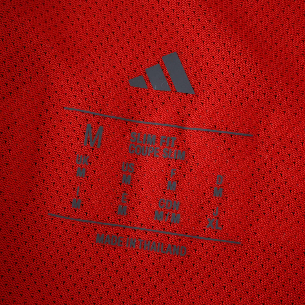 Close-up of Bayern Munich 2025/26 home player version jersey size tag and Adidas logo on red fabric.