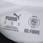 Close-up of the PSV Eindhoven 2025/26 home fan jersey's Puma label showing size and sustainability logos.