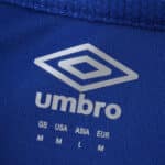 Close-up of the Umbro logo and size chart on the blue Rangers Home 2025/26 Fan Version jersey.