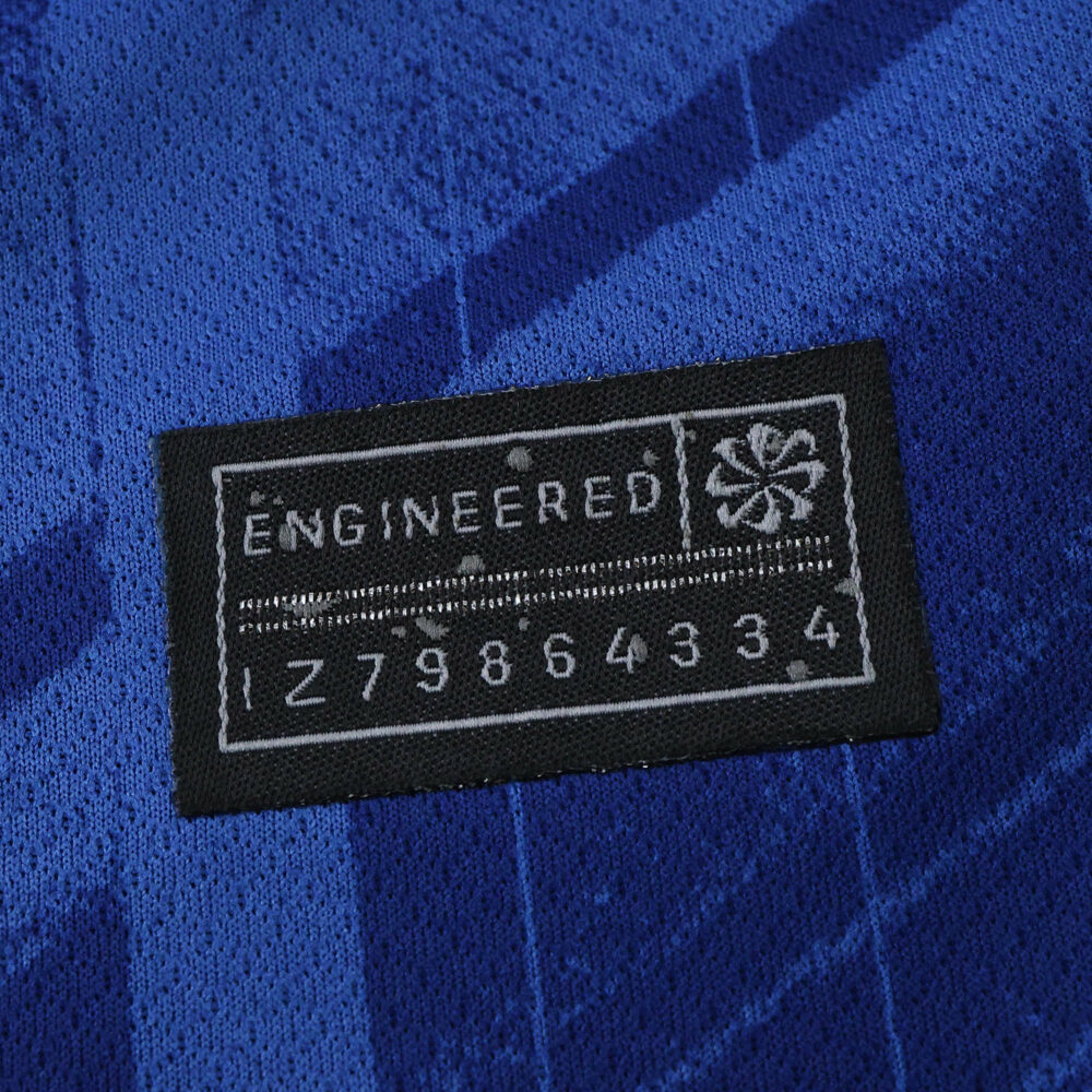Close-up of the "Engineered" label on the 2025/26 Chelsea Home Fan Version jersey in blue fabric.