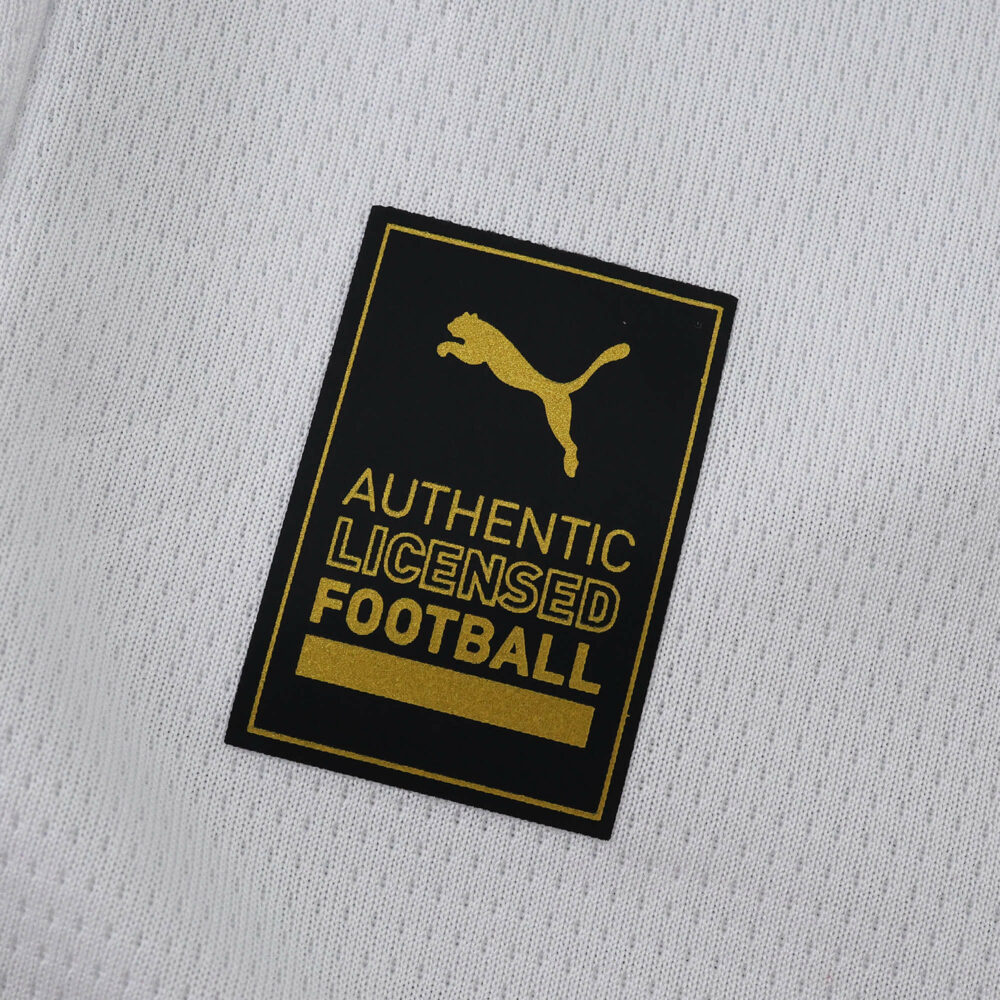 Close-up of the gold and black Puma "Authentic Licensed Football" badge on the Marseille 2025/26 home shirt.
