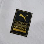 Close-up of the gold and black Puma "Authentic Licensed Football" badge on the Marseille 2025/26 home shirt.