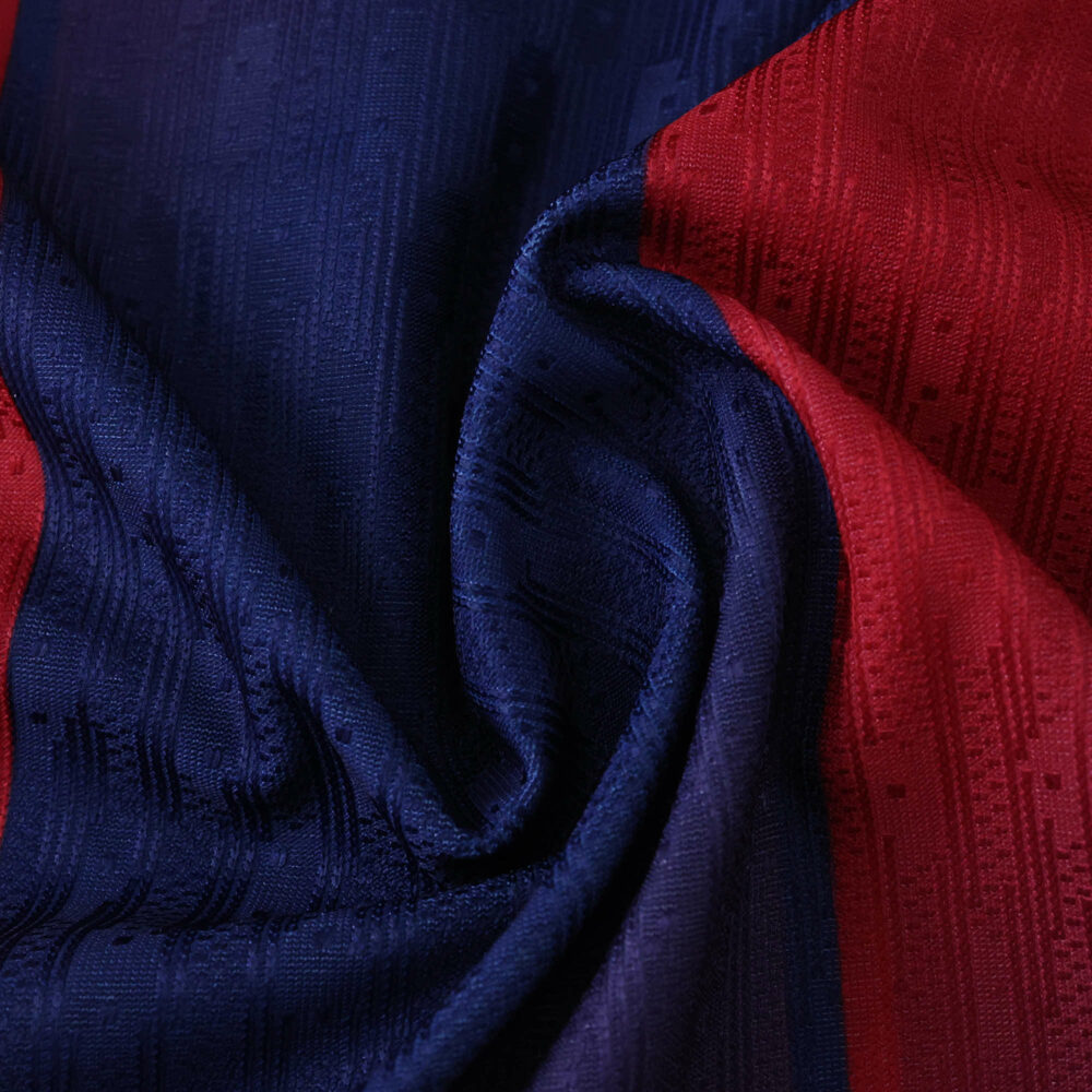 Close-up of 2025/26 Barcelona home jersey fabric showing blue and red colors with textured pattern.