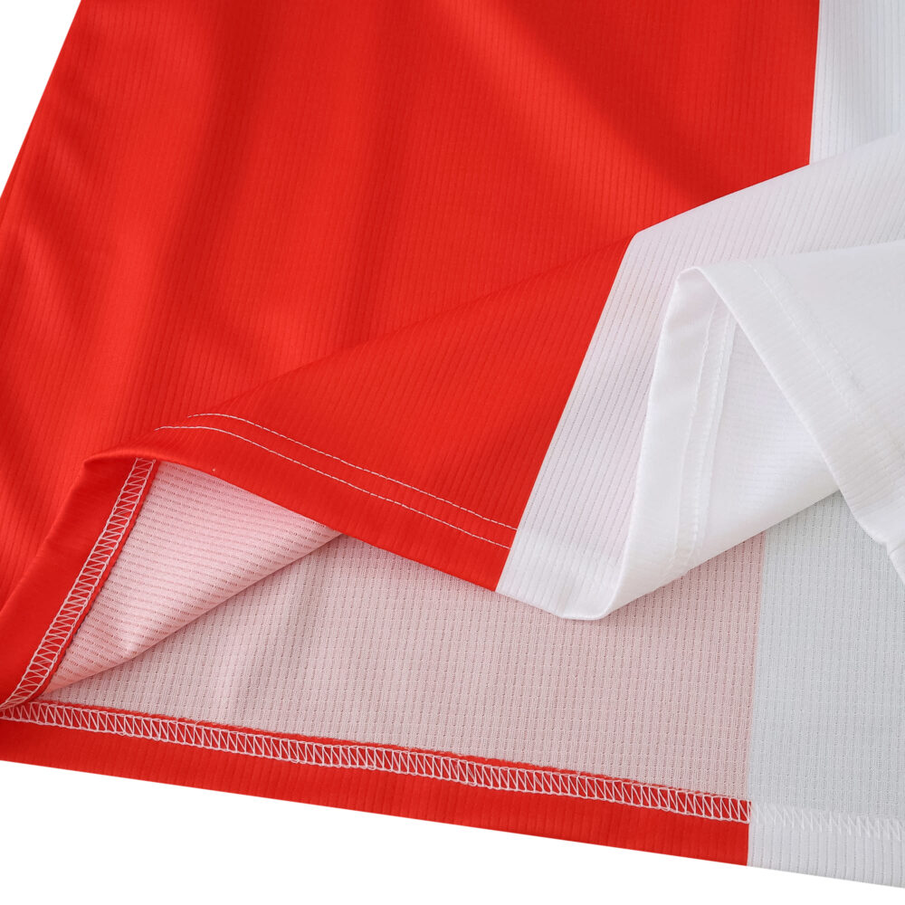 Close-up of Feyenoord 2025/26 home fan jersey fabric, showing red and white color blocks and stitching.