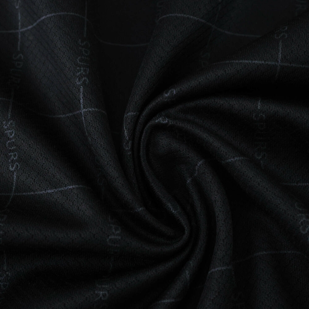 Close-up of Tottenham Hotspur Away 2025/26 fan jersey fabric, showing dark texture and subtle "SPURS" pattern.