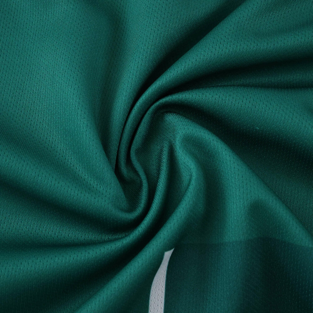 Close-up of Werder Bremen 2025/26 Home fan jersey fabric in green with visible texture and folds.