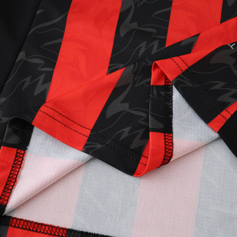 Close-up of AC Milan 2025/26 home jersey fabric showing red and black stripes with textured pattern.