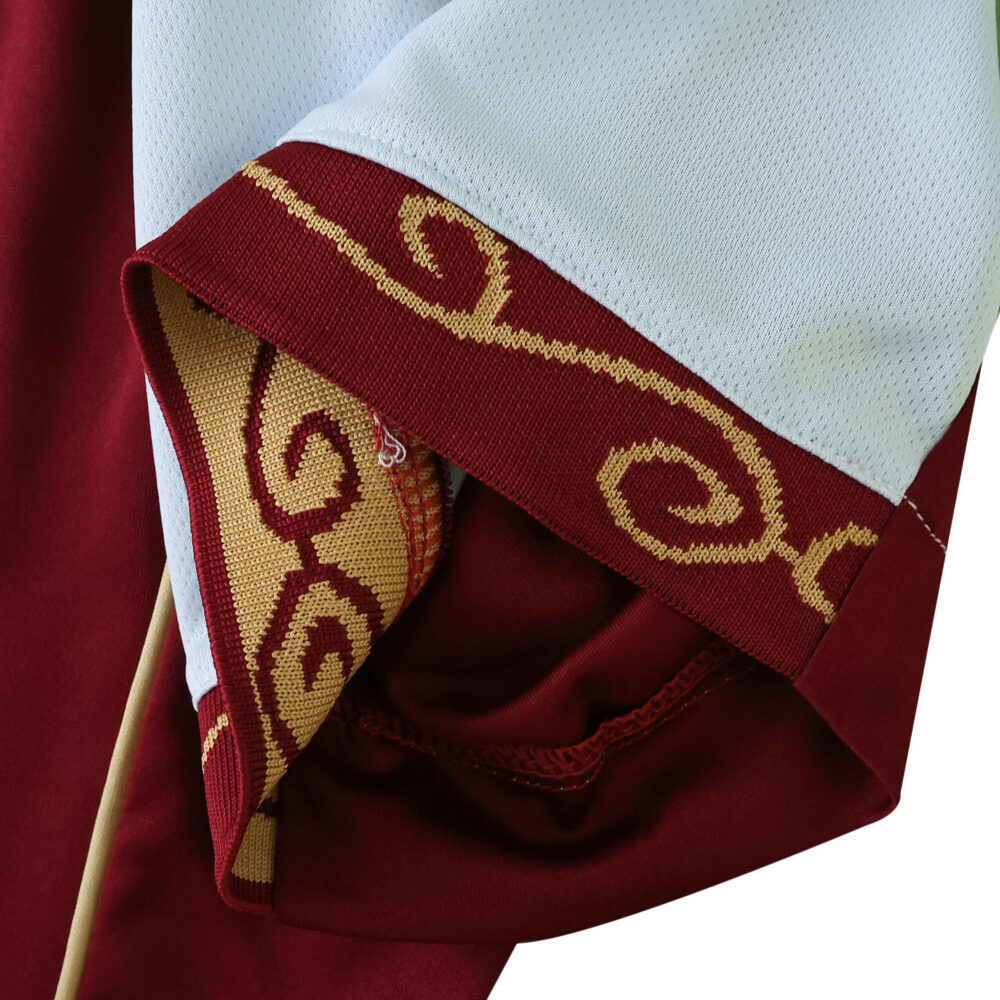 Close-up of Aston Villa 2025/26 home fan jersey sleeve, featuring maroon and gold swirl detailing.