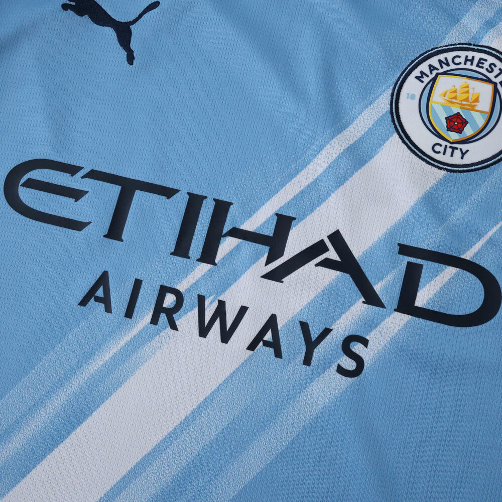 Close-up of the 2025/26 Manchester City home fan jersey showing crest, sponsor, and light blue design.