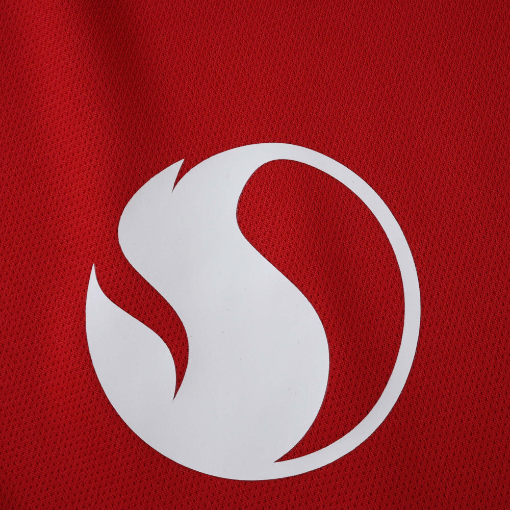 Close-up of the Manchester United 2025/26 home fan jersey featuring a white abstract logo on red fabric.