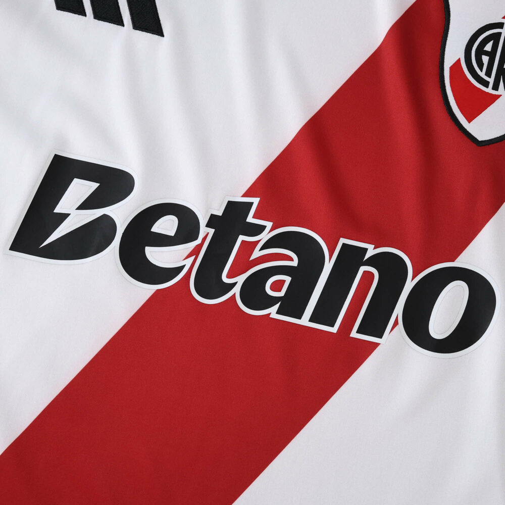 Close-up of River Plate 2025/26 home fan jersey featuring sponsor logo and red diagonal stripe.