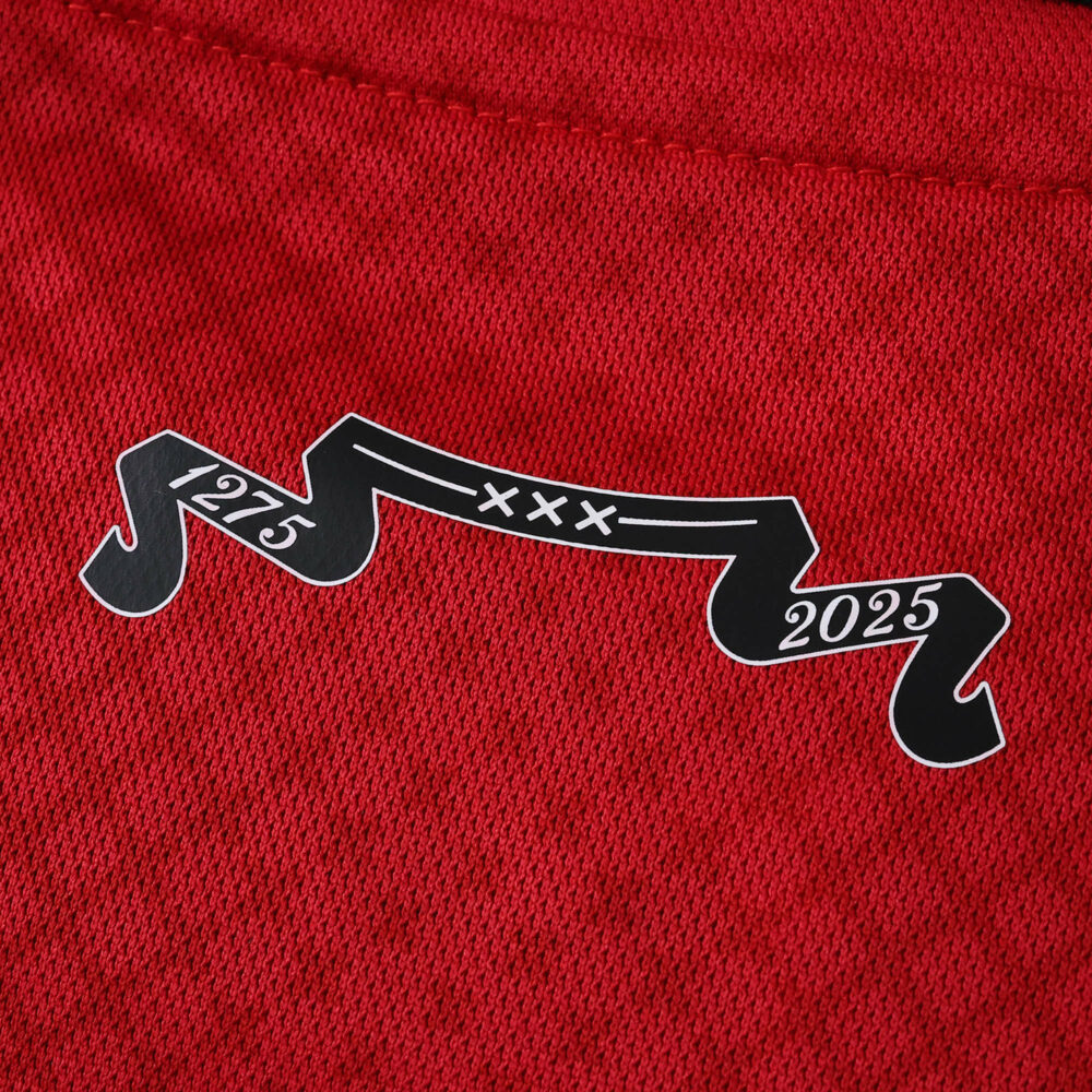 Close-up of a red Ajax 2025/26 fan jersey with a black ribbon showing "1275 XXX 2025" on the fabric.