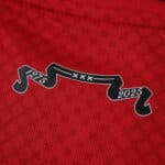 Close-up of a red Ajax 2025/26 fan jersey with a black ribbon showing "1275 XXX 2025" on the fabric.