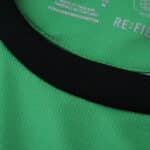 Close-up of the Borussia Monchengladbach 2025/26 away fan jersey's green fabric and black collar trim.