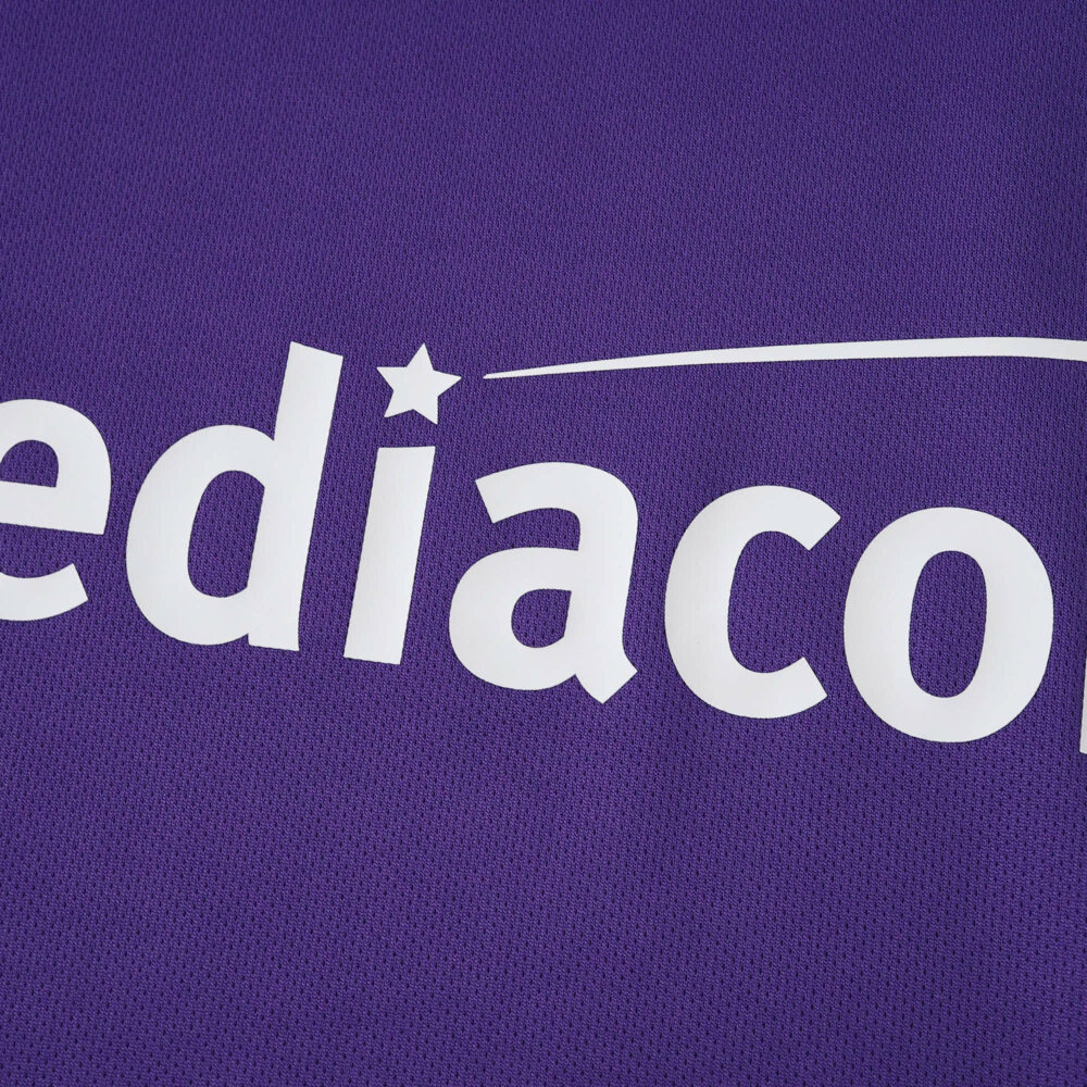 Close-up of Fiorentina 2025/26 home fan jersey showing sponsor logo on purple fabric.