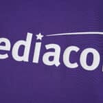 Close-up of Fiorentina 2025/26 home fan jersey showing sponsor logo on purple fabric.