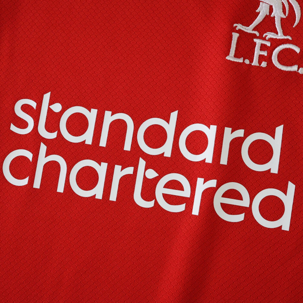 Close-up of the Liverpool 2025/26 Home Fan Version jersey showing logo and Standard Chartered sponsor.