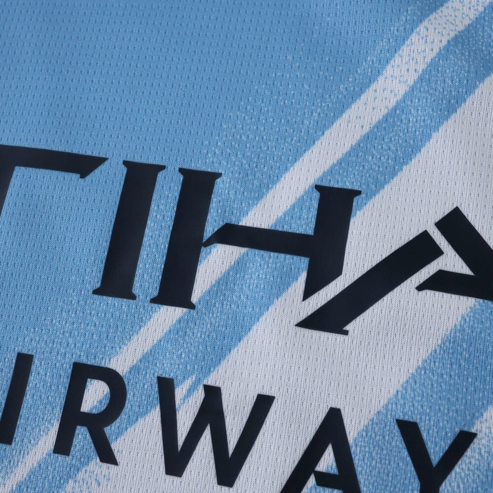 Close-up of the Manchester City 2025/26 home fan jersey showing sponsor text and light blue pattern.