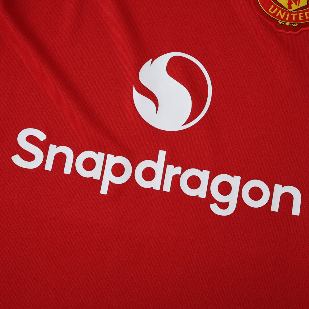 Close-up of the Manchester United 2025/26 home fan jersey with Snapdragon sponsor logo on red fabric.