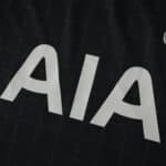 Close-up of the Tottenham Hotspur 2025/26 Away fan jersey showing white "AIA" sponsor text on dark fabric.