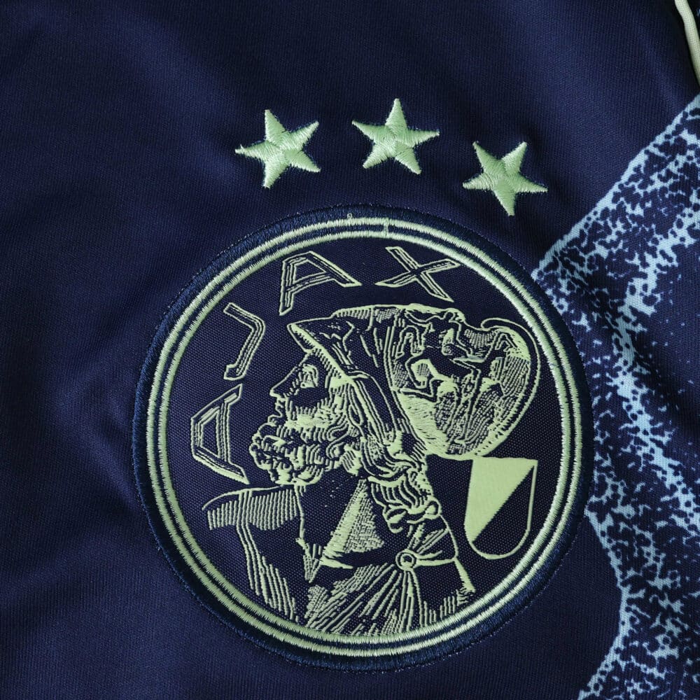 Close-up of the Ajax Away 2025/26 Fan Version jersey featuring the club crest and three stars.