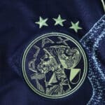 Close-up of the Ajax Away 2025/26 Fan Version jersey featuring the club crest and three stars.
