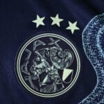 Close-up of Ajax 2025/26 away player version jersey badge with three stars above the club crest.
