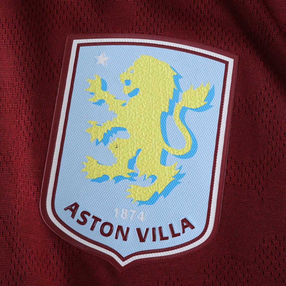 Close-up of the Aston Villa crest on the 2025/26 Home Player Version jersey, maroon fabric background.
