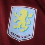 Close-up of the Aston Villa crest on the 2025/26 Home Player Version jersey, maroon fabric background.