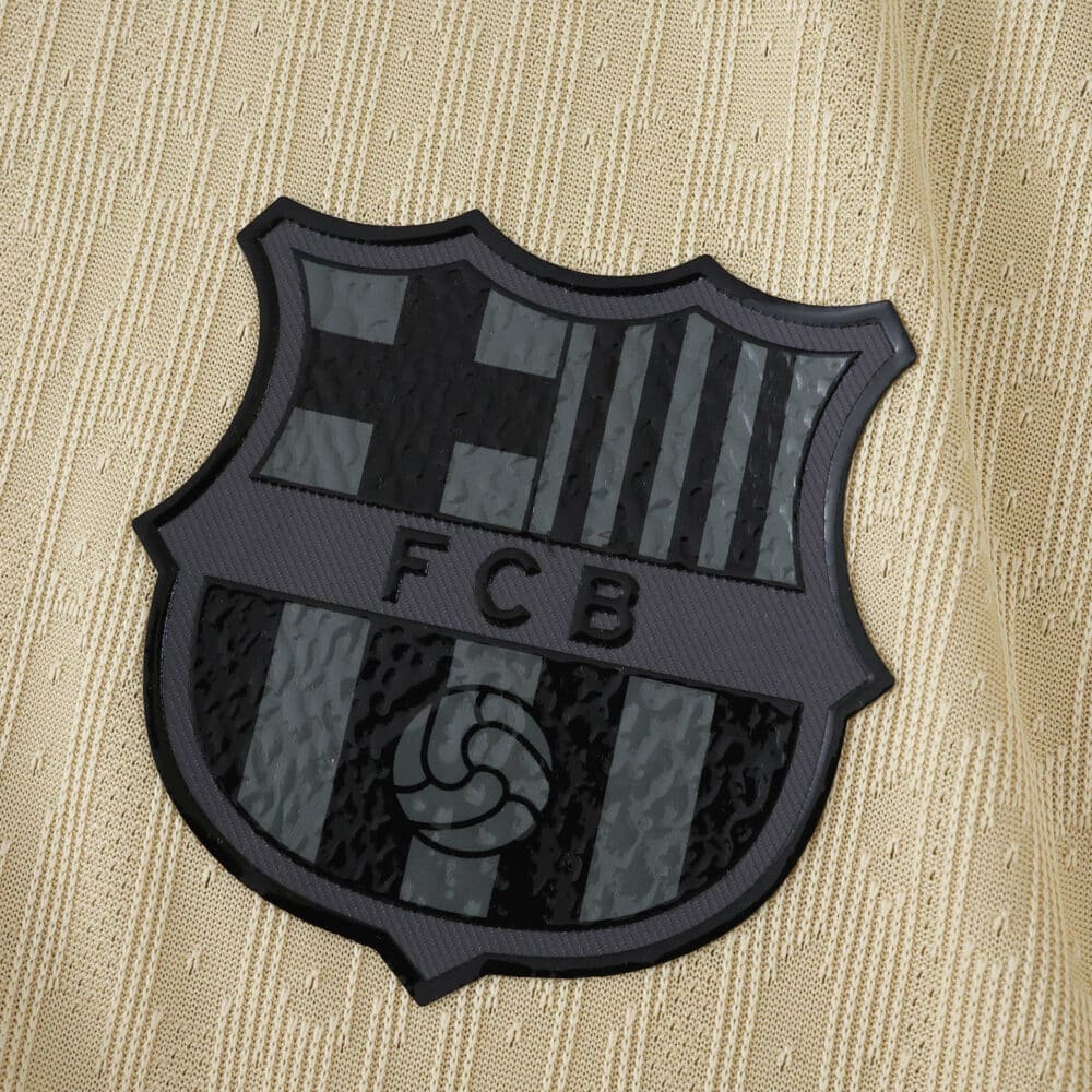 Close-up of the black Barcelona crest on the 2025/26 away player version jersey in gold fabric.