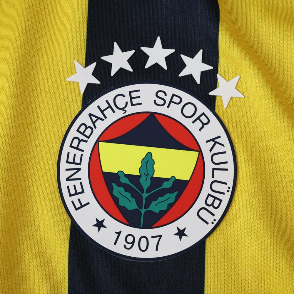 Close-up of Fenerbahce 2025/26 home jersey badge with club crest and stars on yellow and navy fabric.