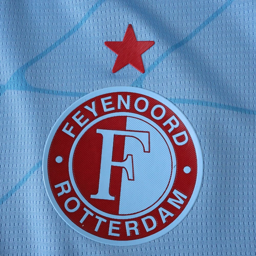 Close-up of Feyenoord crest and red star on the 2025/26 away fan jersey in light blue fabric.