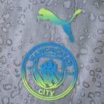 Close-up of the Manchester City 2025/26 third kit with club crest and Puma logo on textured grey fabric.