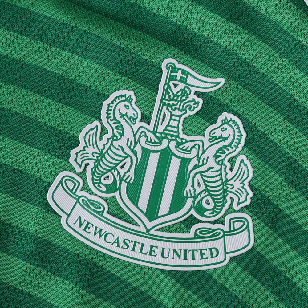 Close-up of the Newcastle United crest on the green striped 2025/26 away player version jersey.