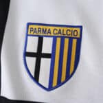 Parma Calcio badge on the 2025/26 home fan jersey, featuring black cross and yellow-blue stripes.